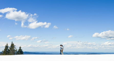 Young Asian couple hold each other, standing on snow at edge of Schafberg mountain (the mountain in movie 'sound of music'), Austria 