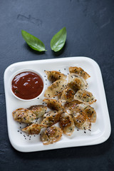 Fried korean wontons with sesame seeds and dipping sauce on a white plate, vertical shot on a black...