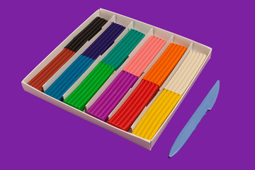 Naklejka premium Set of colorful plasticine sticks lying in a box near a plastic knife on purple background. modeling claying pieces for children play and creativity
