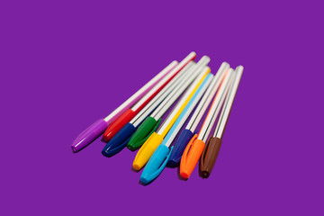 different new bright colored pens lying on a purple background. concept of office supplies