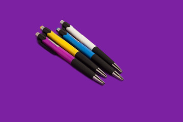 four different new bright colored pens lying on a purple background. concept of office supplies. free copyspae