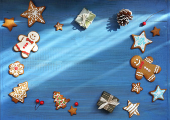 Christmas composition with ginger biscuits on a blue wooden background. Frame of Christmas cookies with gingerbread men, gifts, stars,  fir-trees on wooden table, flat lay, copy space.