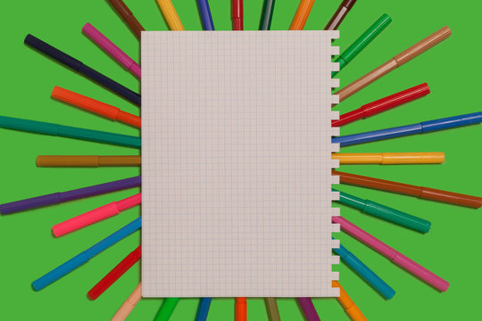 new bright plastic colored felt pens lying under a sheet of paper on a green surface. concept of office supplies. free space for advertising text