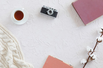 White knitted scarf, cup of tea, notebook, vintage photo camera on white background, top view. Flat lay