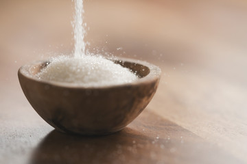 White sugar falling in wood bowl on table