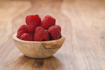 fresh raspberries in wood bowl on table with copy space