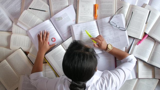 Woman stressed studying in front of many books, letting her head fall down in desperation - Powered by Adobe