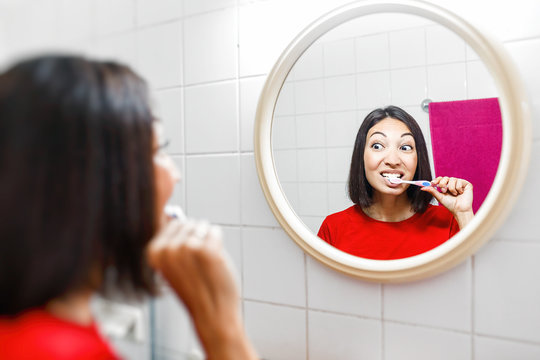 Asian woman brushing teeth and looking in the mirror in the bathroom in her apartment