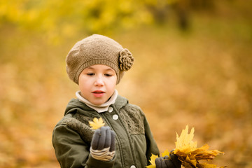 Nice girl in the green hat and coat with yellow leaves in the autumn park