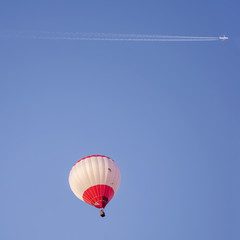 Jet airplane with long white trail  flies over a hot air balloon in a beautiful blue sky