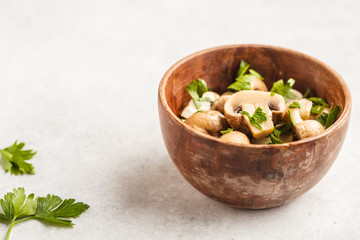 Baked champignons with parsley in wooden bowl.