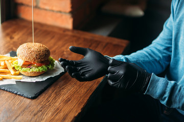 Man in black gloves takes a burger in his hands