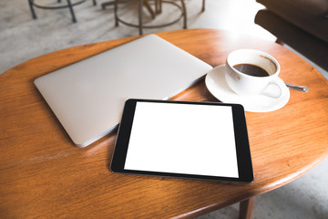 Top view mockup image of a black tablet pc with blank desktop white screen with laptop and coffee cup on wooden table