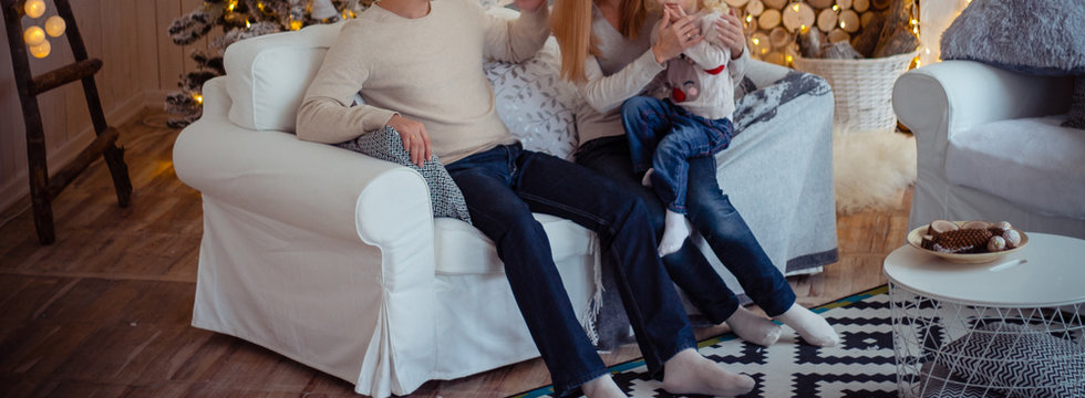 Family On The Couch Near The Christmas Tree. Decorated Living Room With Traditional Fire Place.Cozy Warm Winter Evening At Home.