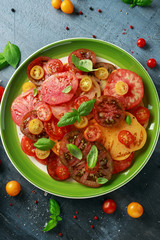 Colorful Tomato Salad with heirloom, pear shaped, beef heart, tigerella, brandywine, cherry, black tomatoes in a green plate. healthy food