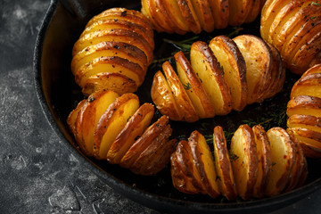 Hasselback baked potatoes served in cast-iron pan with salt, pepper and herbs