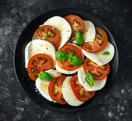 Caprese salad with tomatoes, mozzarella cheese and fresh basil leaves in a black plate. Italian food.
