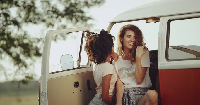African and redhead girls with a good mood smiling and spending a good time sitting in front of the retro orange bus.