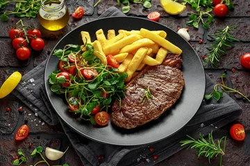 Fototapeten Grilled sirloin steak with potato fries and vegetables, tomato salad in a black plate. rustic table © grinchh