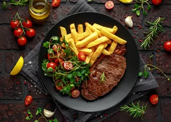 Poster Grilled sirloin steak with potato fries and vegetables, tomato salad in a black plate. rustic table © grinchh