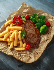 Grilled sirloin steak with potato fries, broccoli and cherry tomatoes on crumpled paper