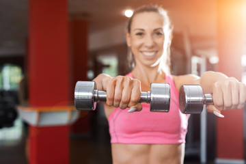 Fototapeta na wymiar slim pretty smiling girl wearing pink and black sportswear doing exercise using dumbbells in a gym. Strength and motivation concept