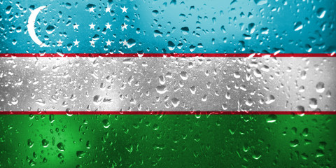 Texture of Uzbekistan flag on the glass with drops of rain.
