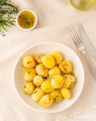 baked in oven with spices round whole potato tubers in plate on white textile background, vertical, top view