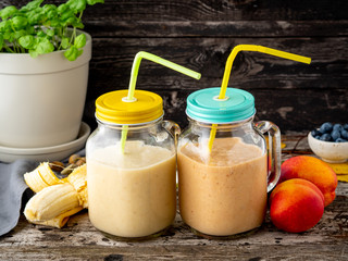 banana peach nectarine smoothie in two jars, fresh fruit milkshakes on old dark rustic wooden table, side view