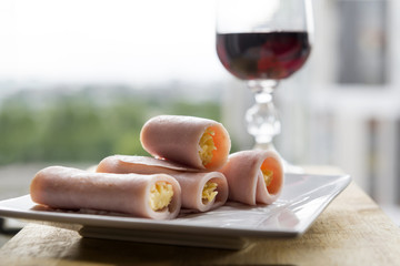 Rolls of ham with cheese filling, glass with red wine, appetizer for wine