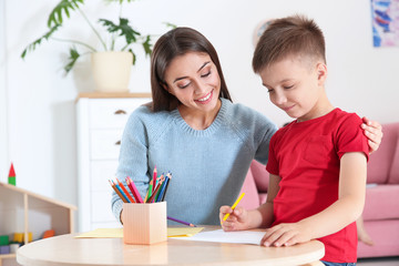 Cute little child drawing at table with his mother in playing room