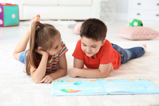 Cute little children reading book on floor in playing room