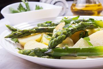 Boiled potato with grilled green asparagus on white plate. Close up.