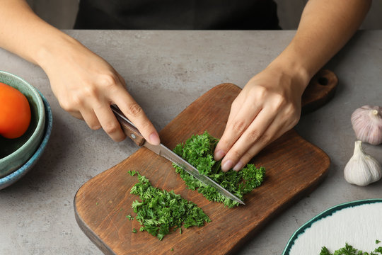 Woman cutting fresh green parsley on wooden board, closeup