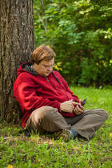 A fat man is sitting on the grass with a phone in his hands