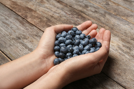 Woman holding juicy fresh blueberries on wooden table
