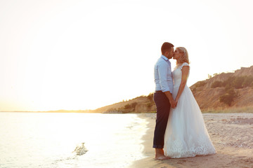 Fototapeta na wymiar Wedding couple holding hands and kissing on beach. Space for text