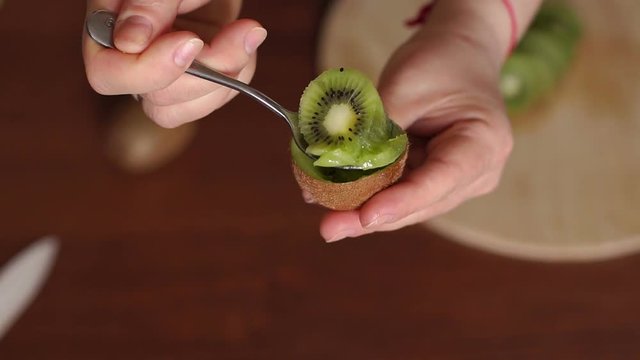 Girl is eating ripe kiwi with tea dessert spoon. Demonstration of fruit. Concept of nutrition, healthy, beauty and diet. Girl is eating kiwi with a tea spoon on wooden background.