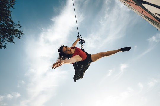 Sexy dancer performing aerial dance on urban scenery at sunset against blue sky