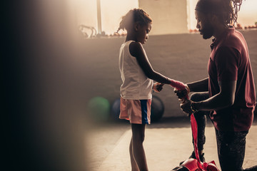 Coach wrapping a bandage on the hands of a kid boxer