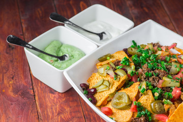 A plate of delicious nachos with jalapeno, beans and guacamole sauce