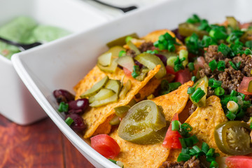 A plate of delicious nachos with jalapeno, beans and guacamole sauce
