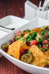 A plate of delicious nachos with jalapeno, beans and guacamole sauce