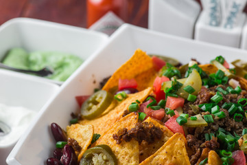 A plate of delicious nachos with jalapeno, beans and guacamole sauce