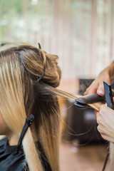 Fototapeta premium The hairdresser pulls the client hair, after washing his head, applying nutrients to the hair and drying the hair with a hair dryer, botox hair, restoring and nourishing the hair