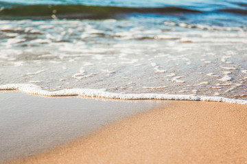 waves of pure azure water with white foam on yellow sand on a sunny day, close up blurry background