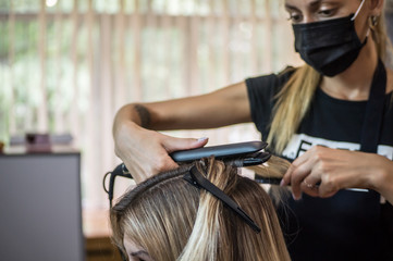 Naklejka premium The hairdresser pulls the client hair, after washing his head, applying nutrients to the hair and drying the hair with a hair dryer, botox hair, restoring and nourishing the hair