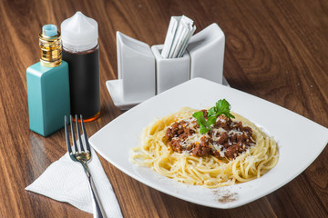 Spaghetti Bolognese and vaporizer on wooden background