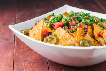 A plate of delicious nachos with jalapeno, beans and guacamole sauce