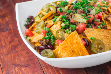 A plate of delicious nachos with jalapeno, beans and guacamole sauce